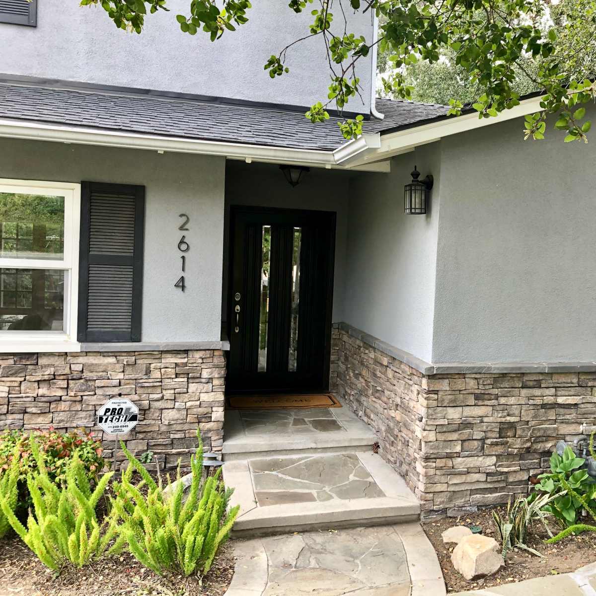 A home entrance with a gray facade, stone accents, and a landscaped pathway leading to the front door.