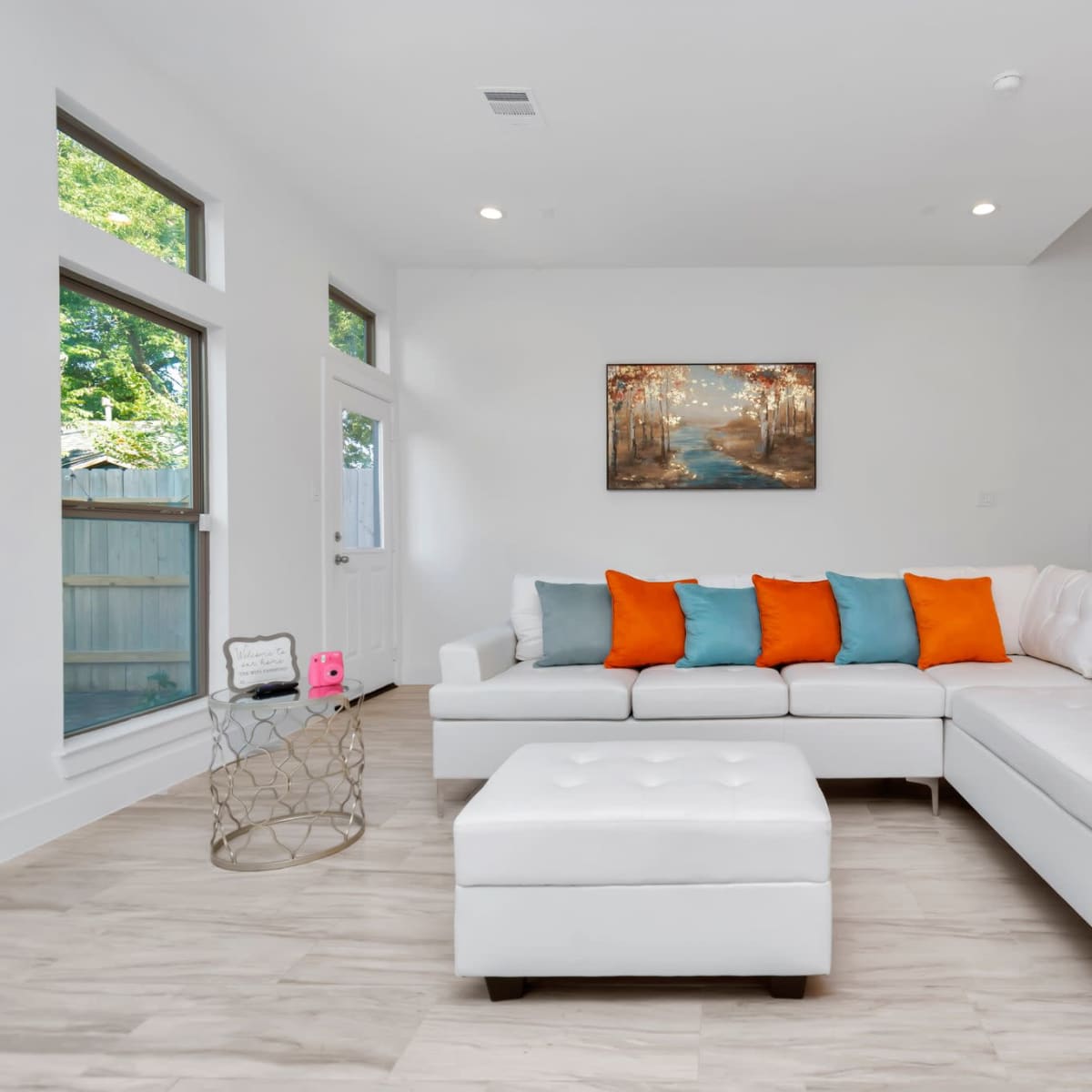 A modern living room with a white sectional sofa, colorful pillows, a small decorative table, and a staircase in the background.