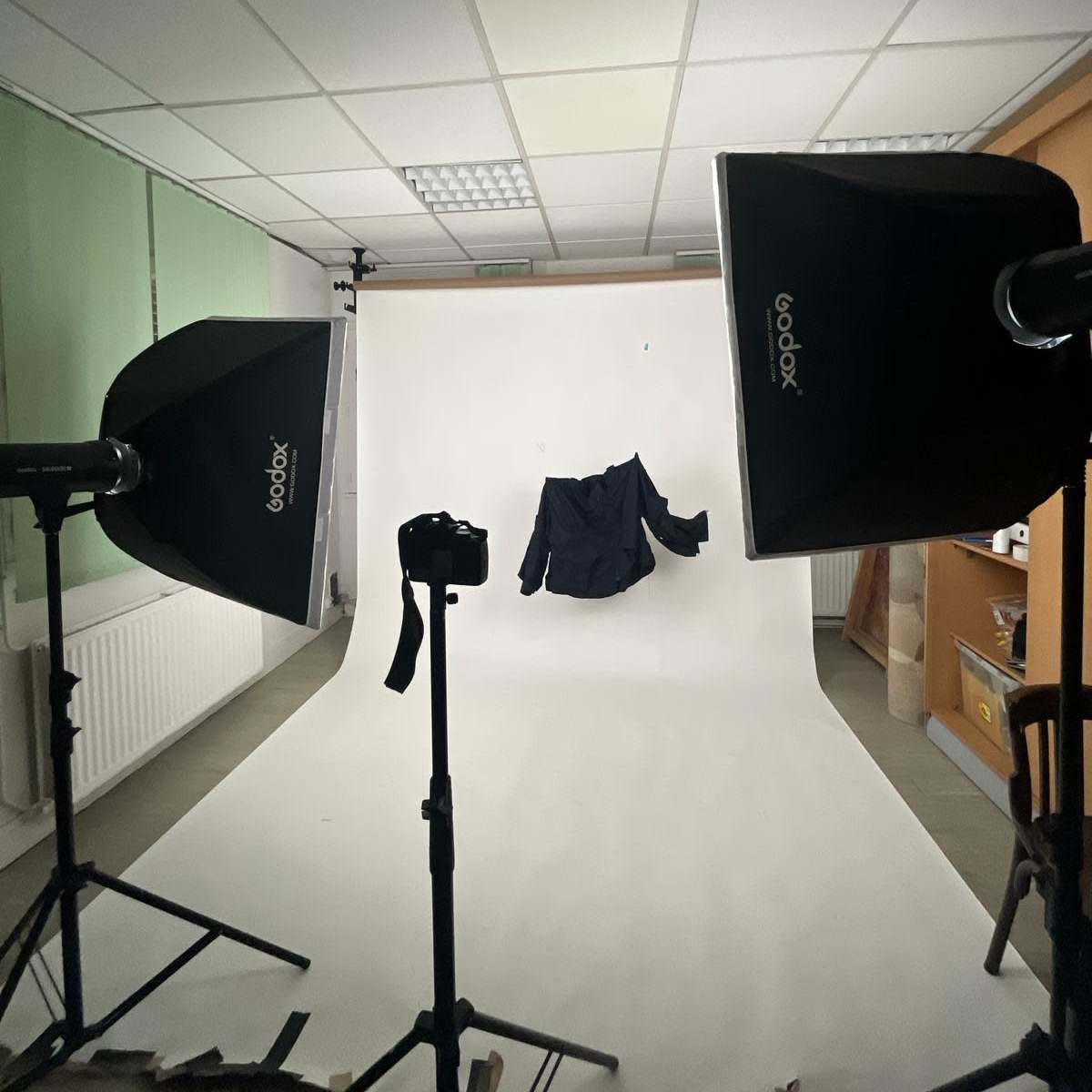 A photography setup with two lights pointing towards a hanging jacket against a plain white backdrop.