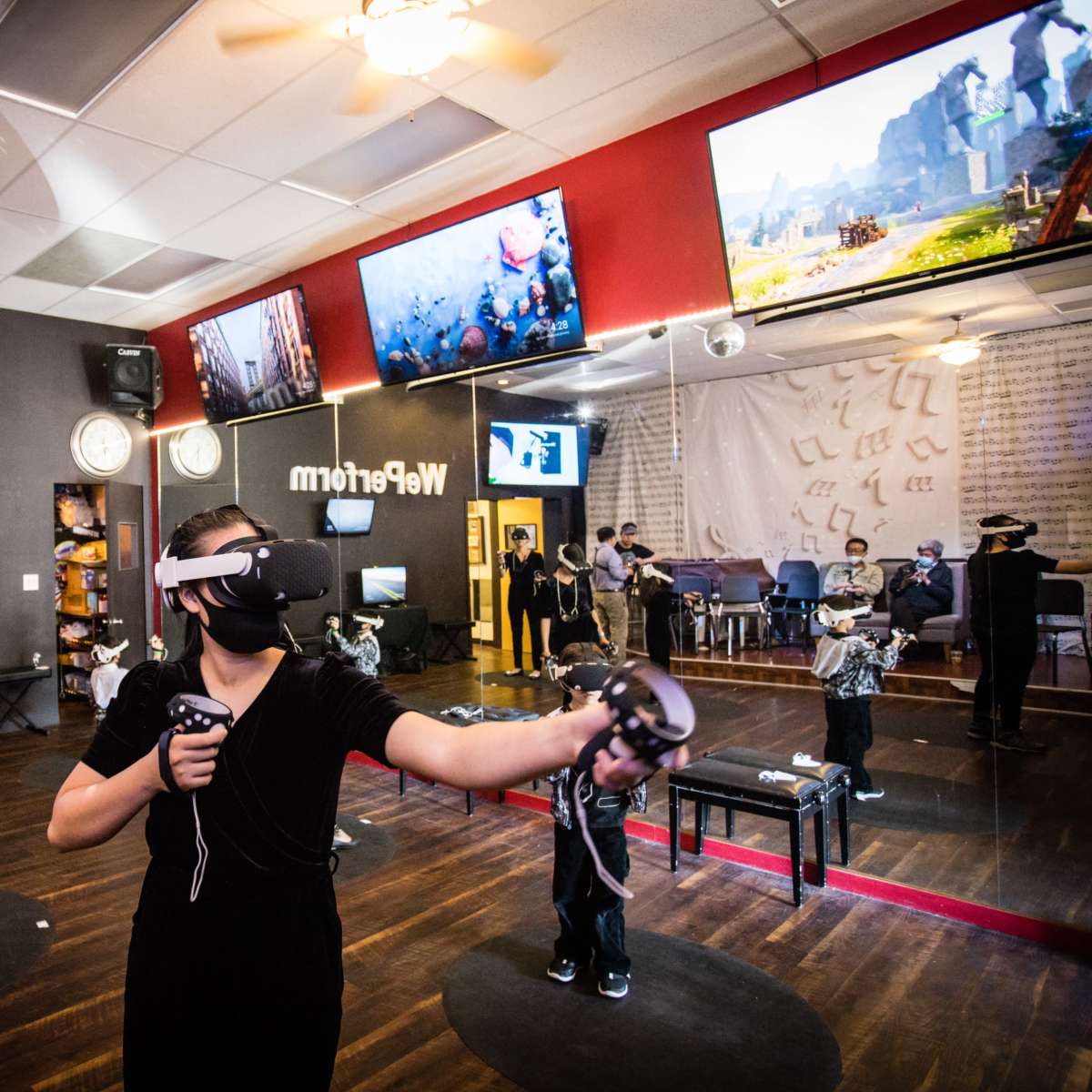 A group of people wearing virtual reality headsets engage in immersive experiences in a studio with large screens and a mirrored wall.