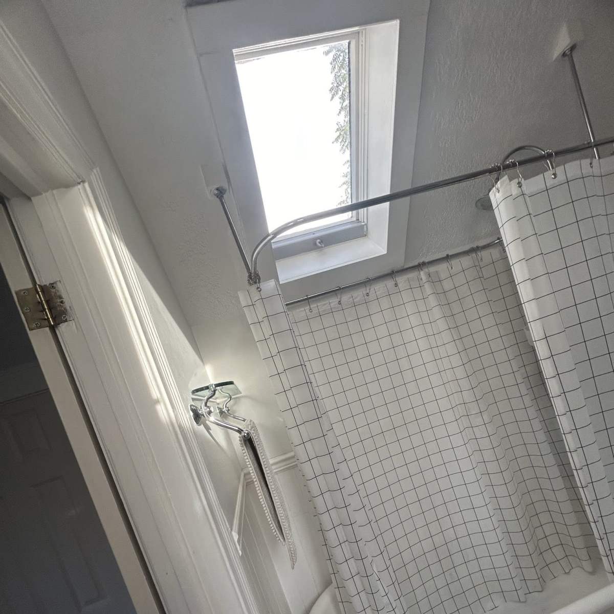 A bathroom with a skylight above a clawfoot bathtub, surrounded by a shower curtain.