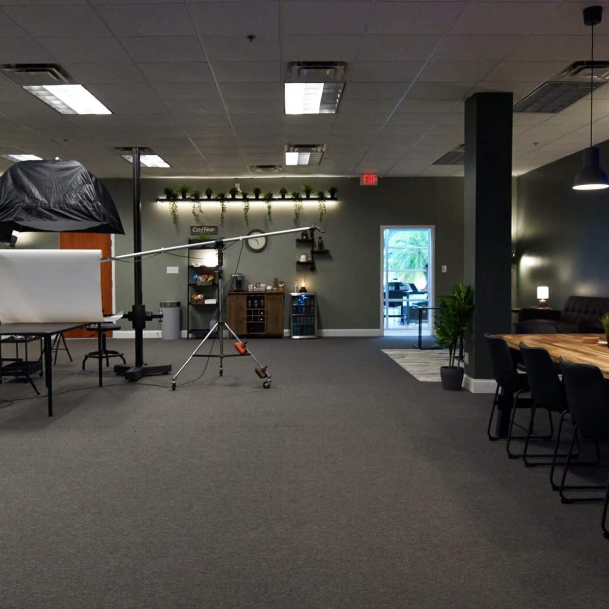A spacious studio with a photography setup on one side and a dining area with a long wooden table and chairs on the other.