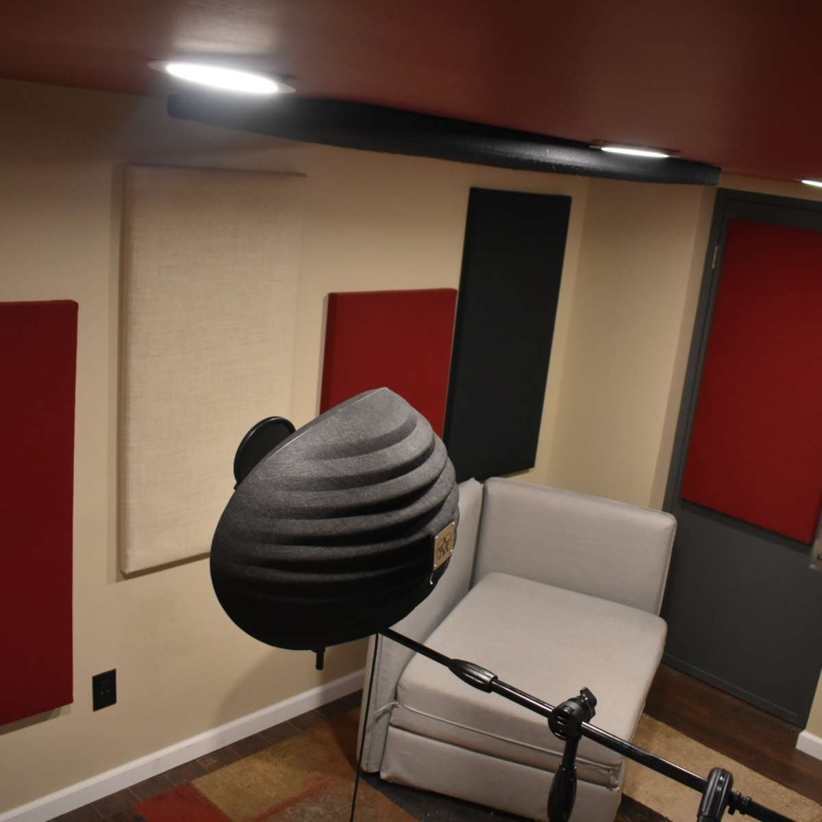 A soundproof recording studio featuring a microphone, a gray couch, and sound-absorbing panels on the walls.