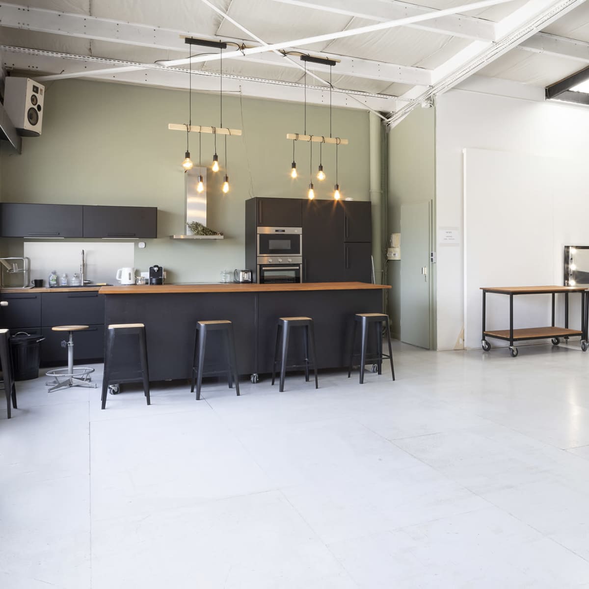 A spacious, modern kitchen and living area with a bar counter, stools, and a gray sofa against the wall.