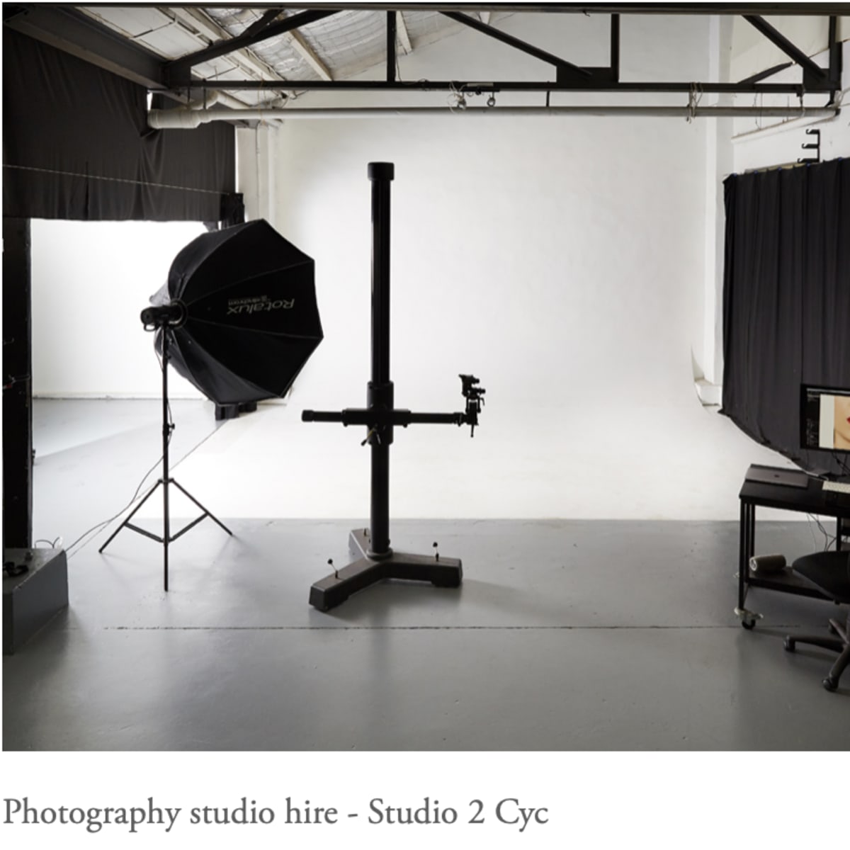 A photography studio equipped with a backdrop, lighting setup, and a computer workstation.