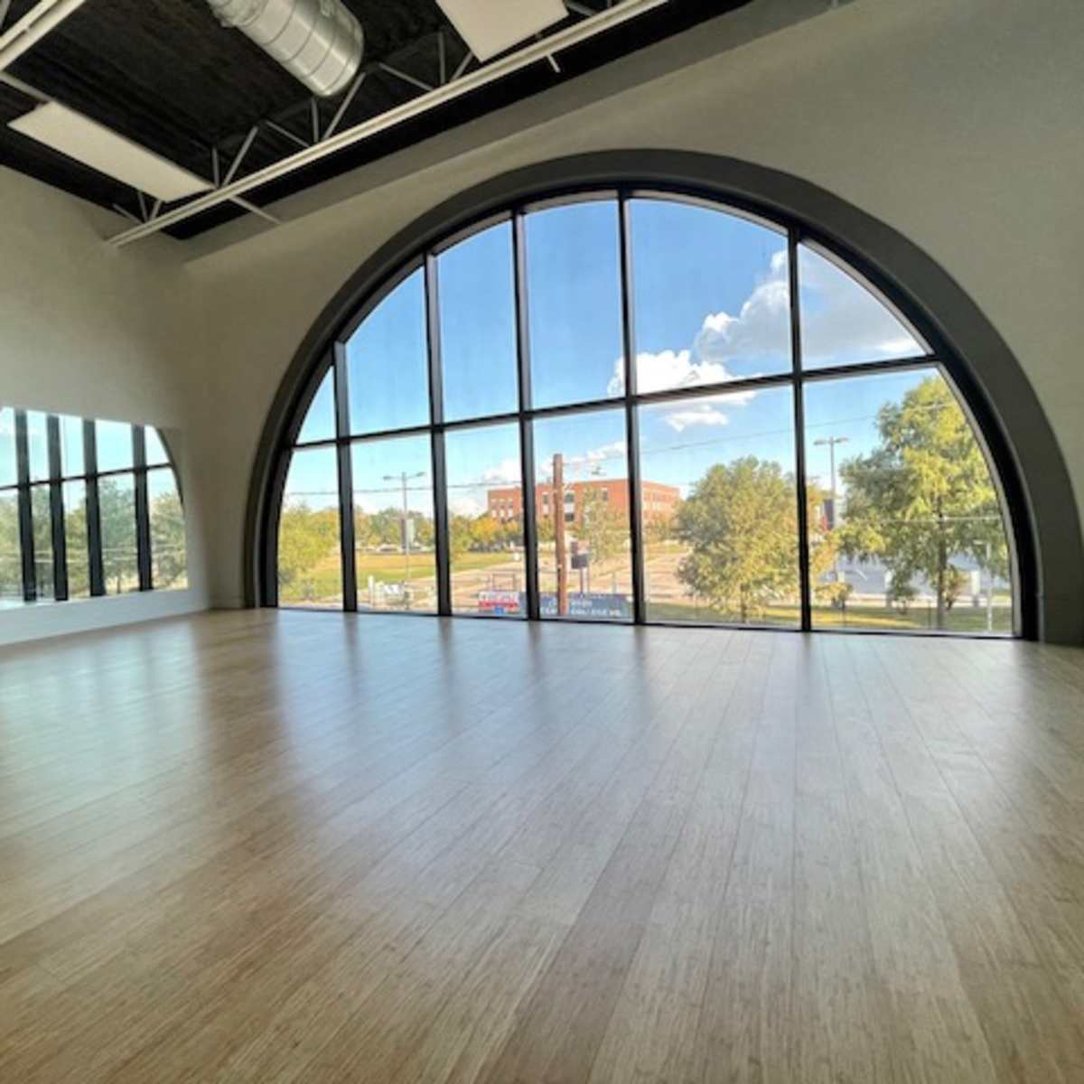 A spacious interior with large arched windows overlooking a street and trees outside.