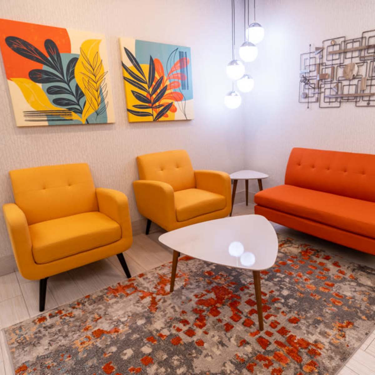 A modern seating area with two yellow chairs, an orange sofa, a white tabletop, and abstract wall art.