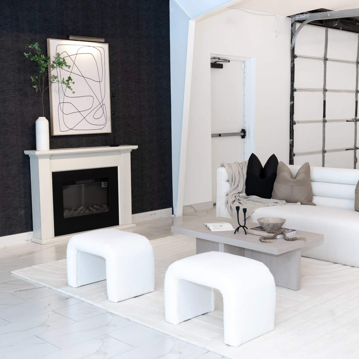 A modern living room with a white sofa, a coffee table, and a fireplace surrounded by dark wallpaper and light-colored flooring.