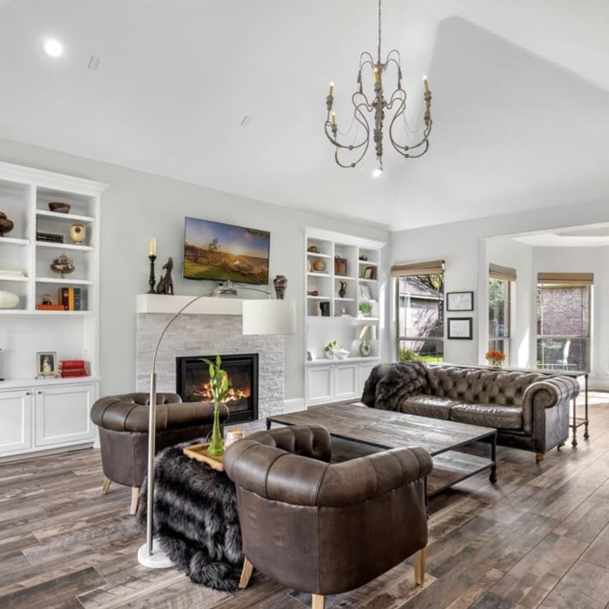 A spacious living room featuring a leather sofa, wooden flooring, and built-in bookshelves filled with decorative items.