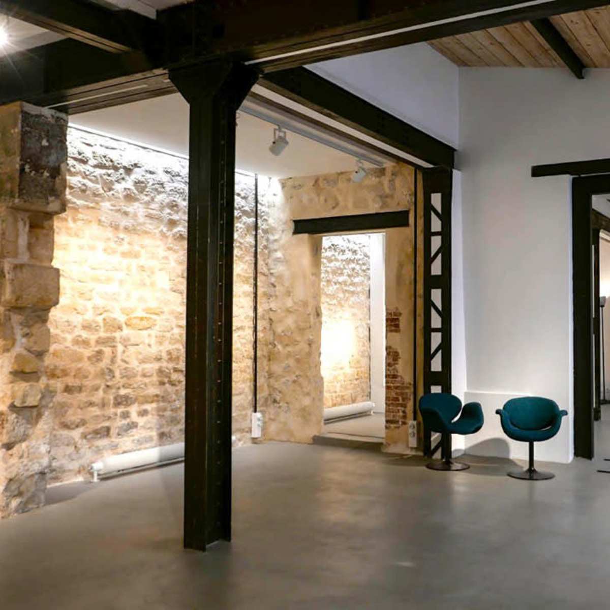 An interior space with exposed stone walls, high wooden ceilings, and modern furniture arranged in a minimalist design.