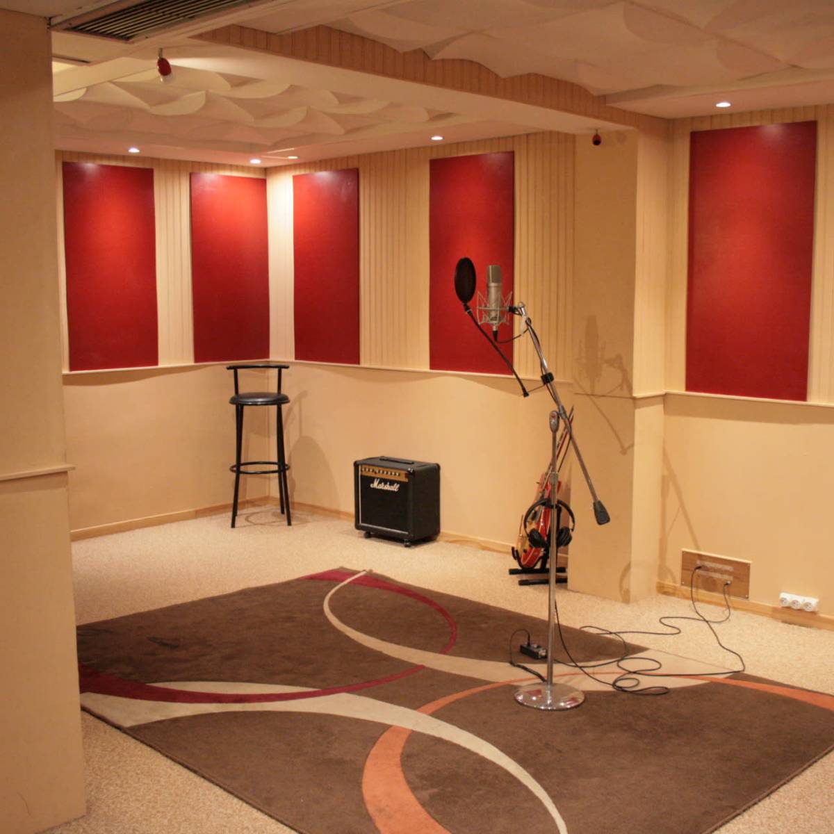 A sound studio with red-accented walls, a microphone on a stand, an amplifier, and a carpeted area.