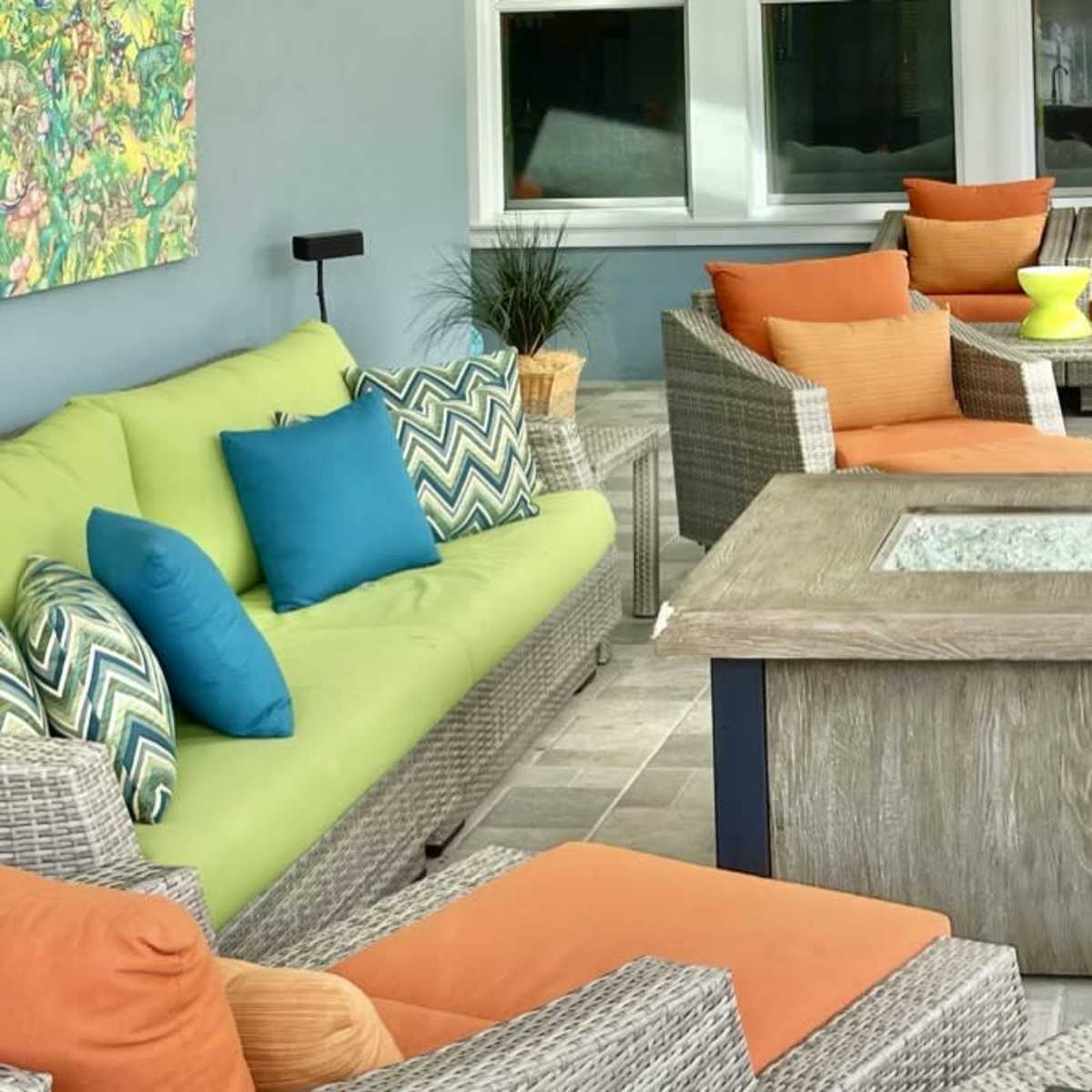 A cozy outdoor seating area with colorful cushions on wicker furniture surrounding a square table with a glass top.