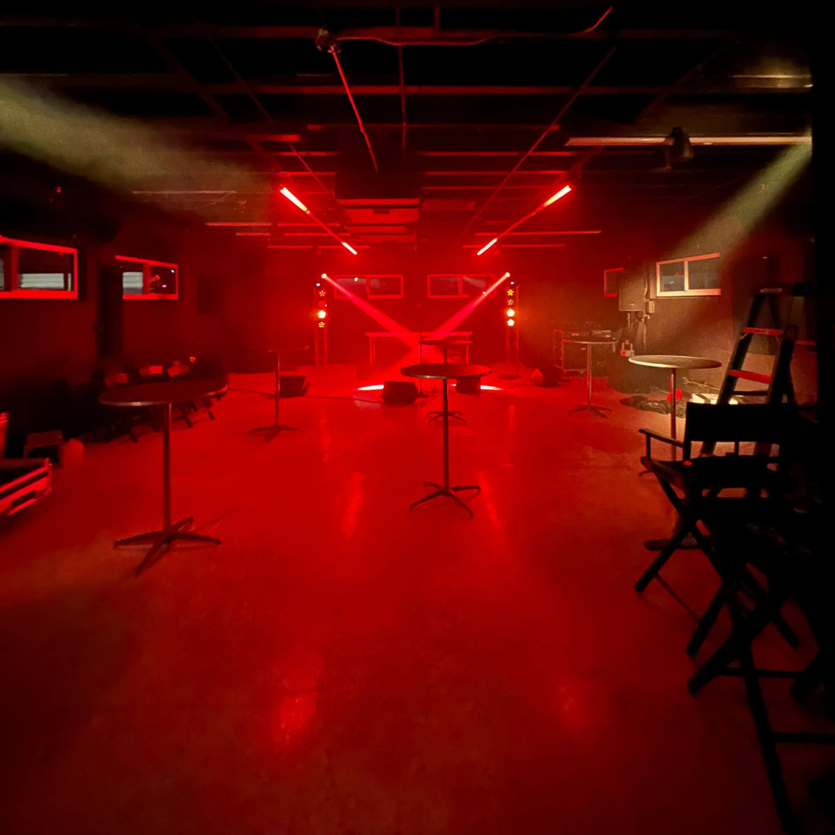 An empty venue with red lighting and several tall tables arranged throughout the space.