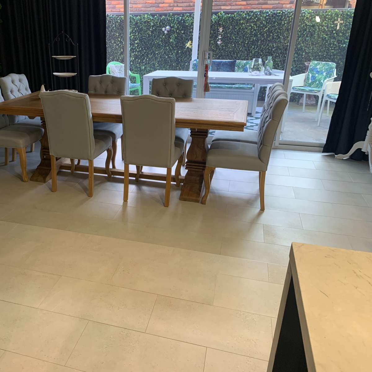 A dining area with a large wooden table surrounded by six upholstered chairs, with a sliding glass door leading to an outdoor patio in the background.