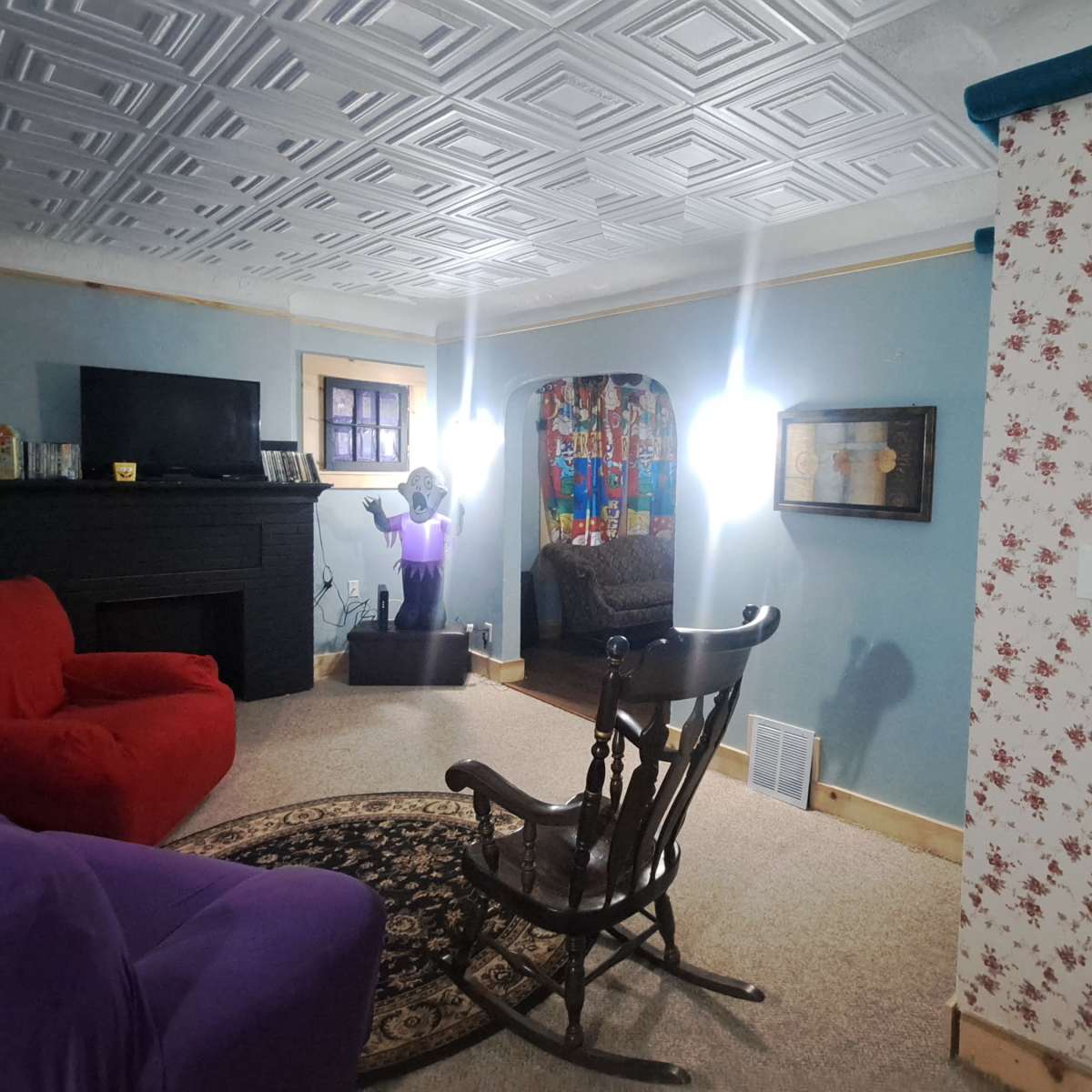 A living room with a red and purple sofa, a rocking chair, a fireplace, and floral wallpaper.