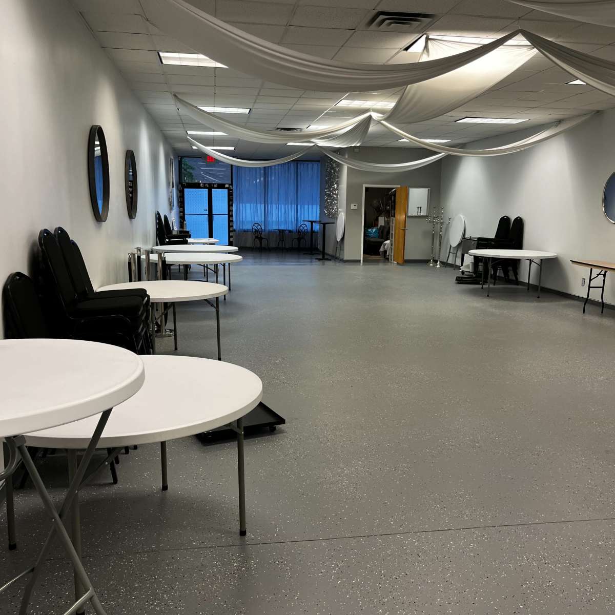 A spacious, empty room with white walls, folding tables, and draped fabric overhead.