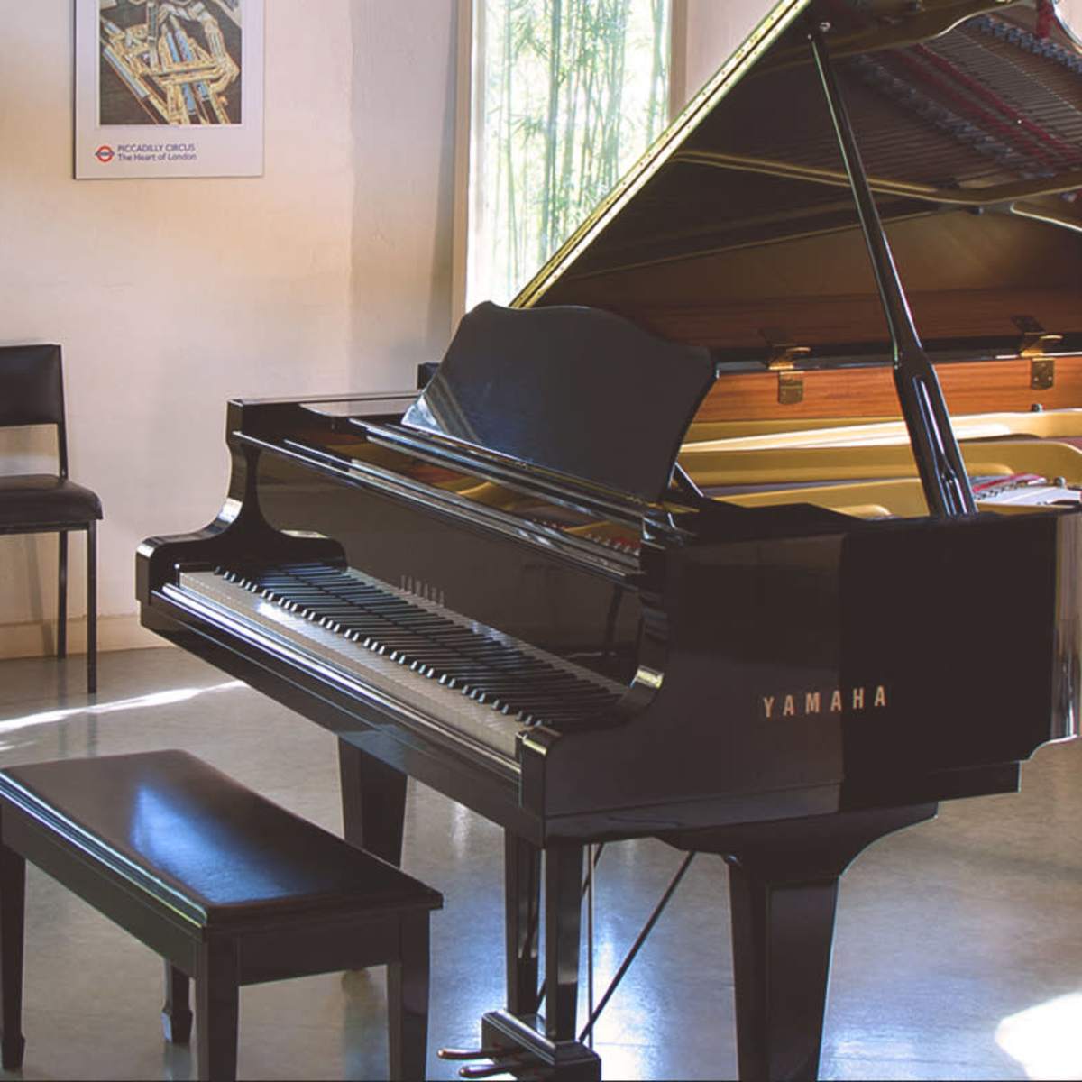 A grand piano is positioned in a well-lit music room with chairs and artwork on the walls.