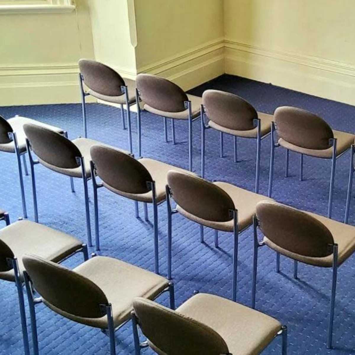 A row of gray chairs is arranged in a semi-circle on a blue carpet in a spacious room.