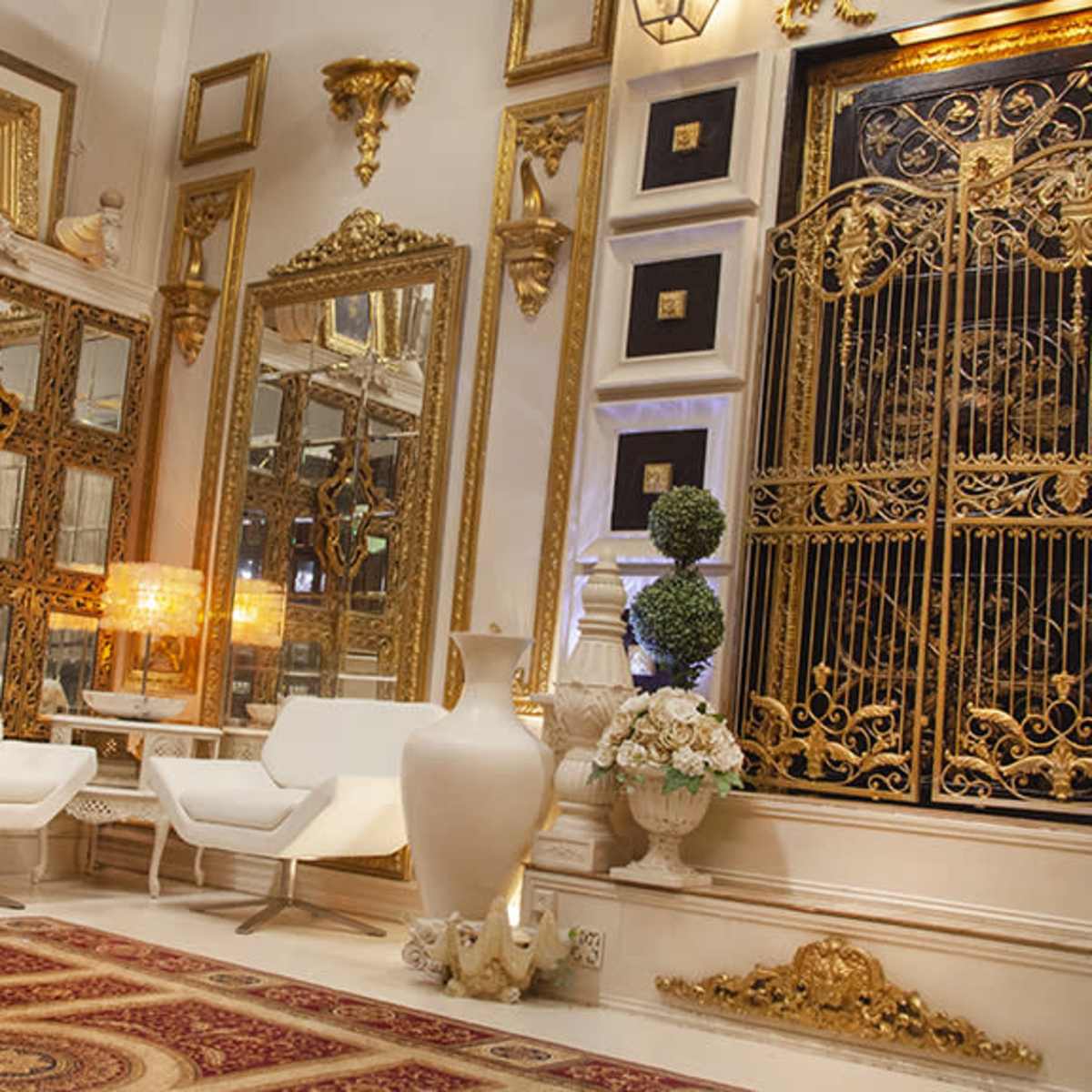 An elegantly decorated room featuring ornate mirrors, a golden wrought iron gate, plush seating, and intricate decorative elements.