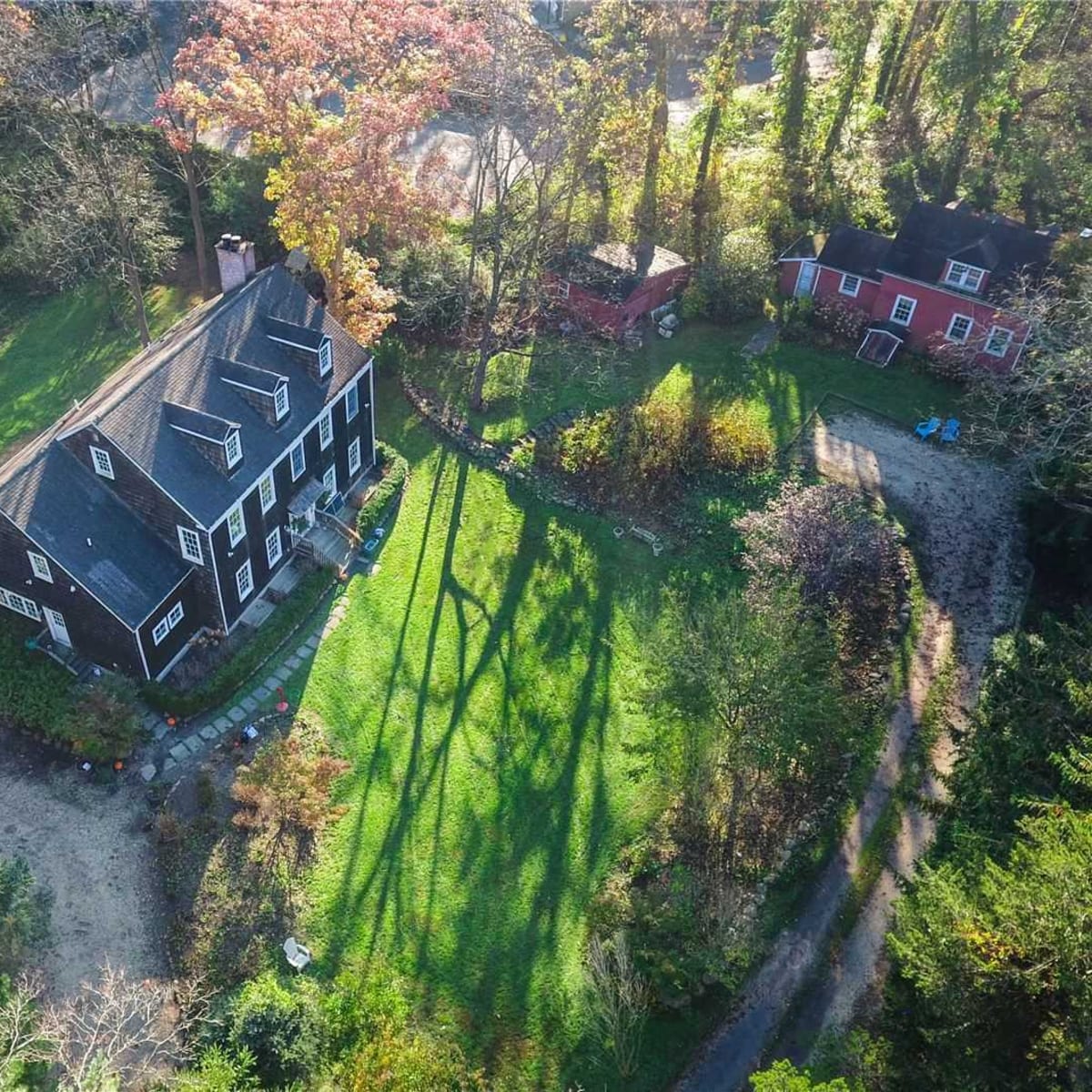 An aerial view shows a large black house surrounded by green lawns and trees, with a smaller red house visible in the background.