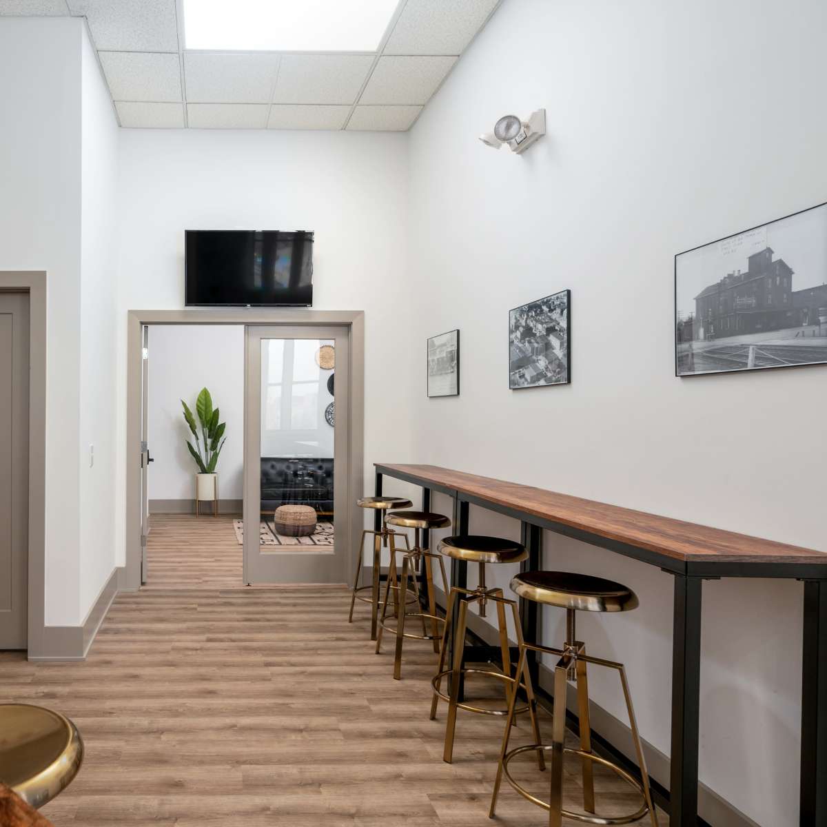 A modern hallway featuring bar stools along a wooden counter, a television mounted on the wall, and a door leading to a separate room.