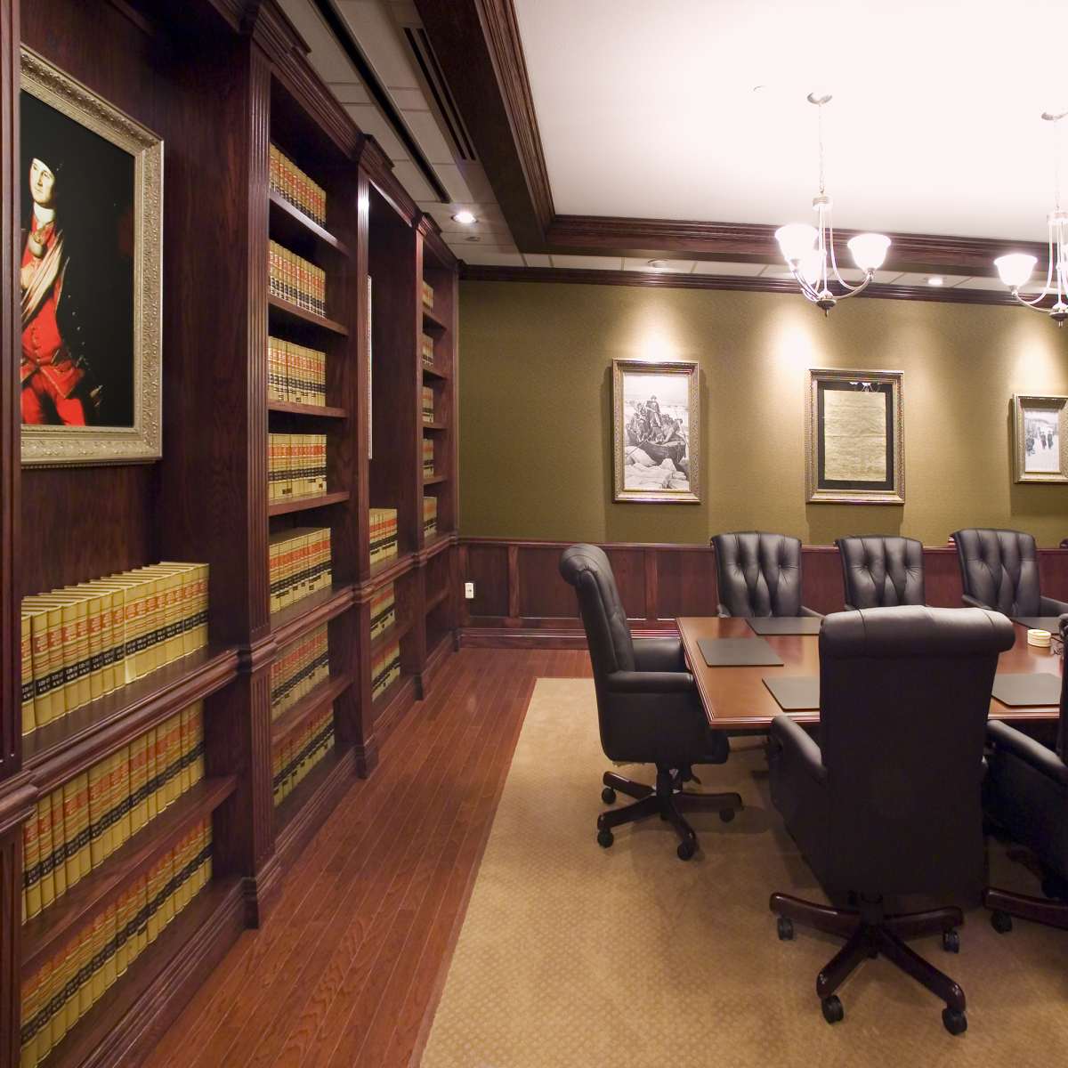 A formal conference room with dark wood paneling, a long table surrounded by black leather chairs, and shelves filled with law books.