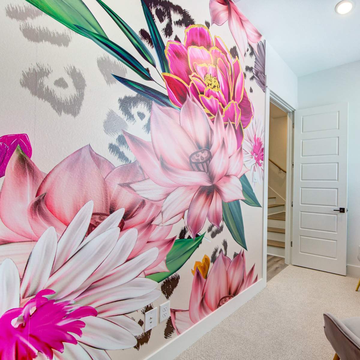 A brightly decorated corner features a floral mural on one wall, with two chairs and a small table beside a door leading to a stairway.