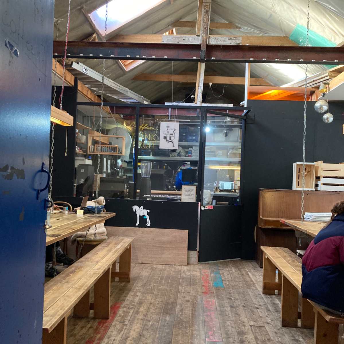 A rustic interior of a workshop or studio with wooden benches, a black wall, and large windows letting in natural light.