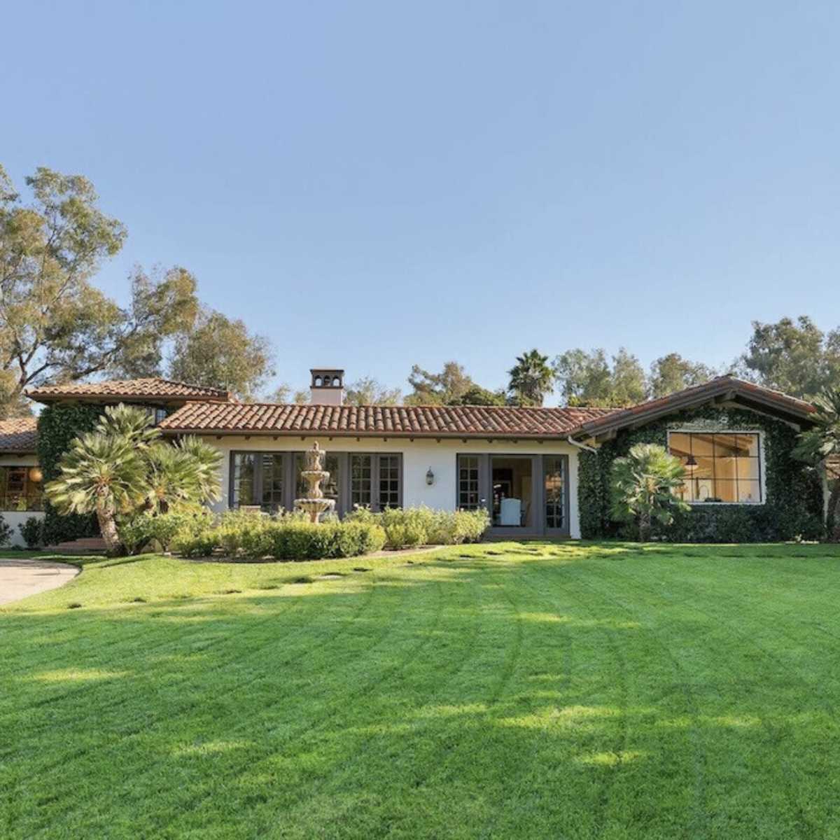 A single-story house with a tiled roof is situated on a well-maintained lawn surrounded by trees and shrubs.
