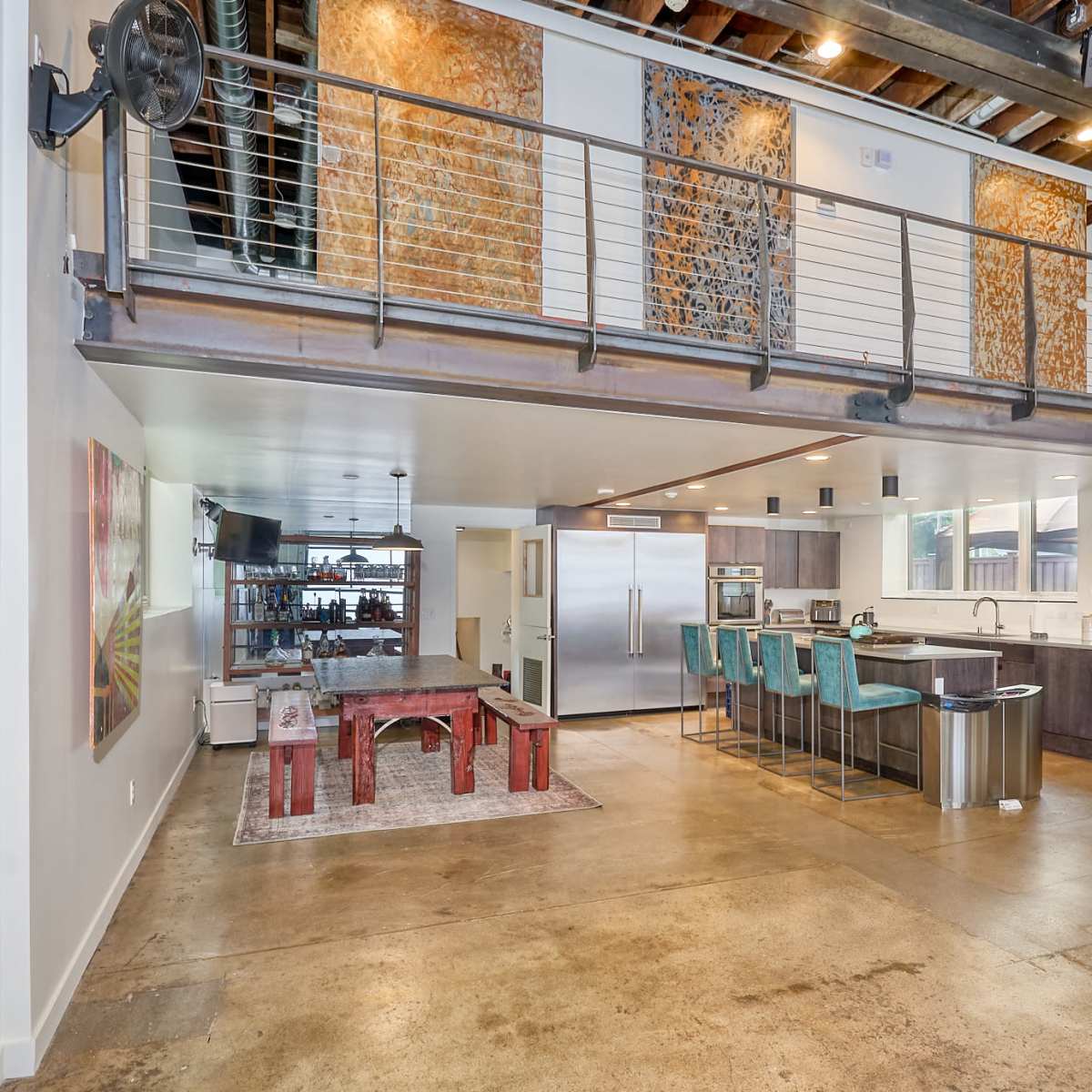 A modern open-concept kitchen and dining area with exposed wood beams, a large island with bar seating, and industrial-style decor.
