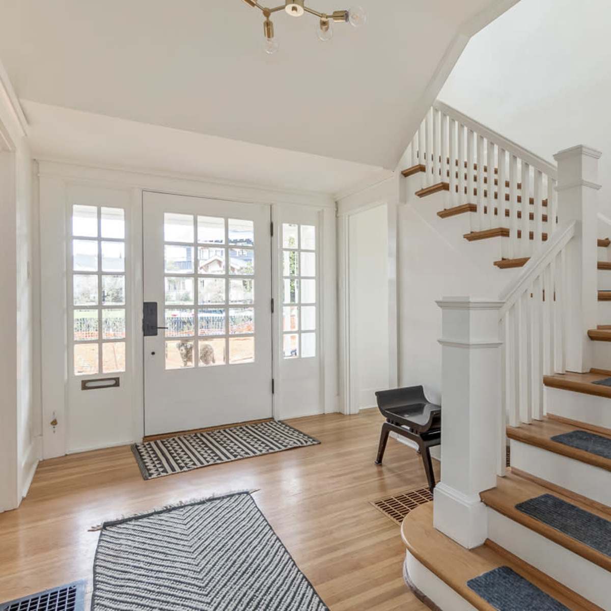 The entrance hall features a staircase, decorative rugs, and a large front door with sidelights.