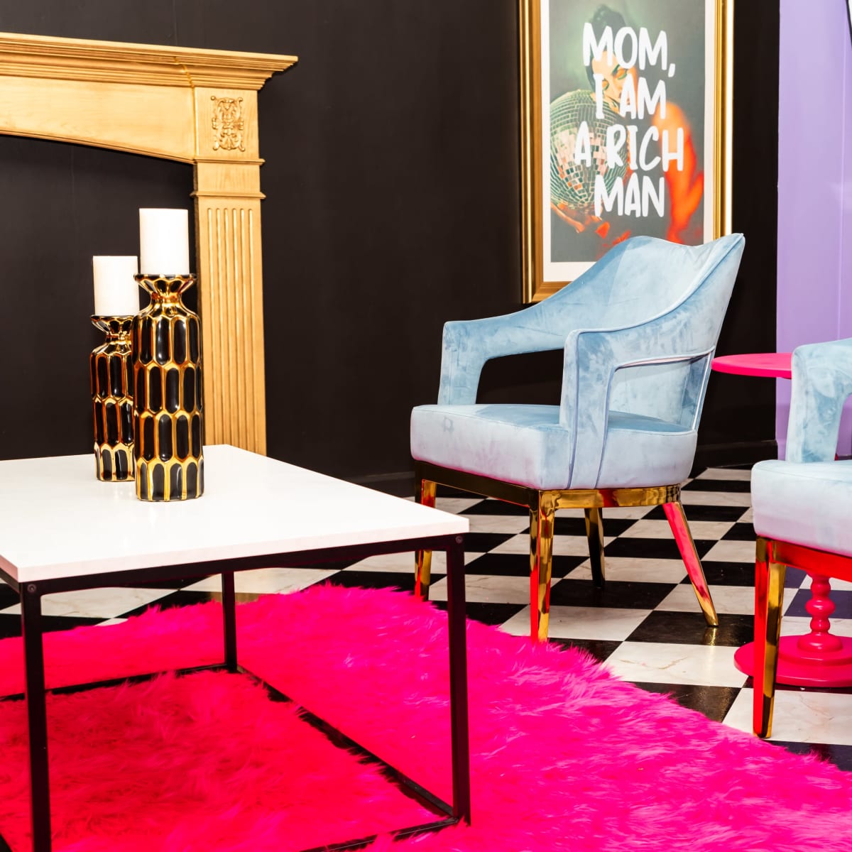 A vibrant interior scene features two blue armchairs with gold legs, a white table, and a pink rug set against a black and white checkered floor.