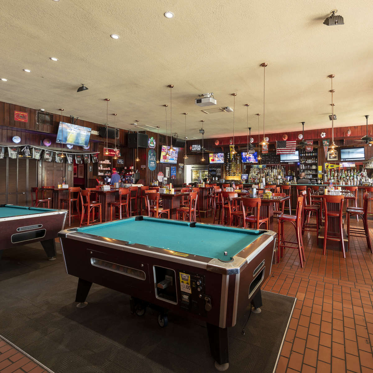 The interior of a bar with pool tables, bar stools, and several televisions mounted on the walls.