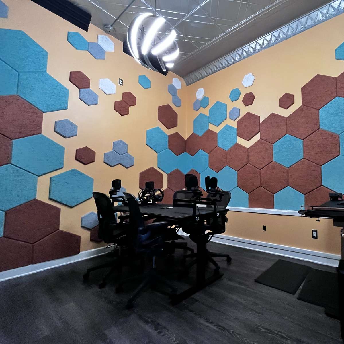 The room features a modern design with hexagonal wall panels in various colors and a central table equipped with multiple chairs and computer setups.