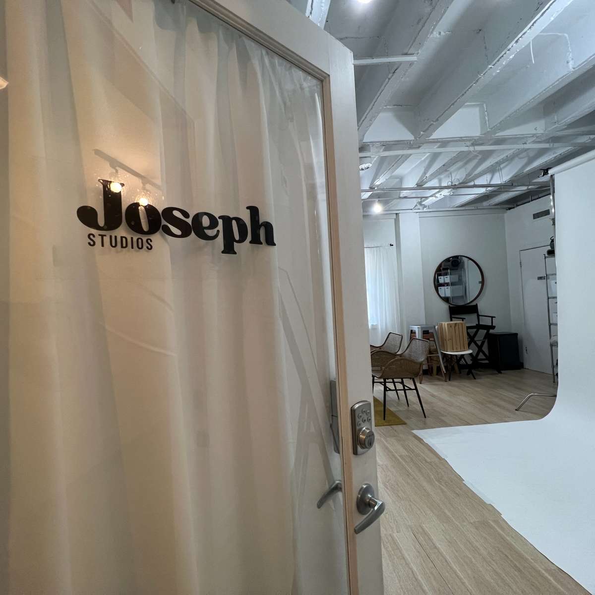 A door with "Joseph Studios" written on it, leading into a well-lit studio space featuring a white backdrop and various furniture.