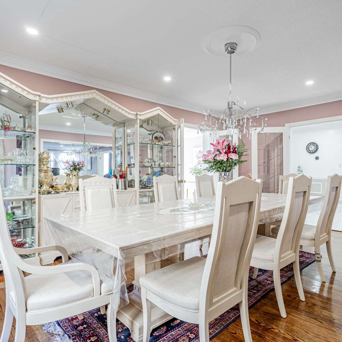 A spacious dining room with a large table surrounded by chairs, a chandelier overhead, and display cabinets filled with decorative items along the walls.