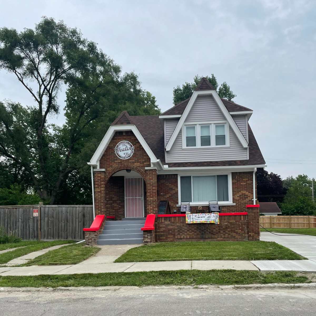 A brick house with a gabled roof features red steps and a sign above the entrance.