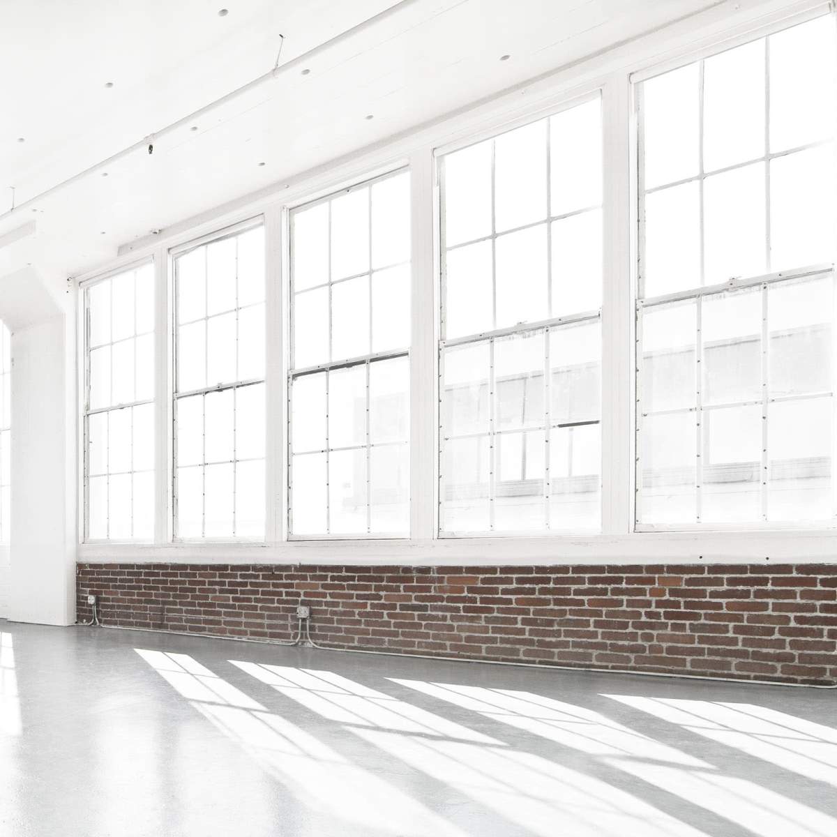 A spacious room with large windows and a brick wall, filled with natural light.