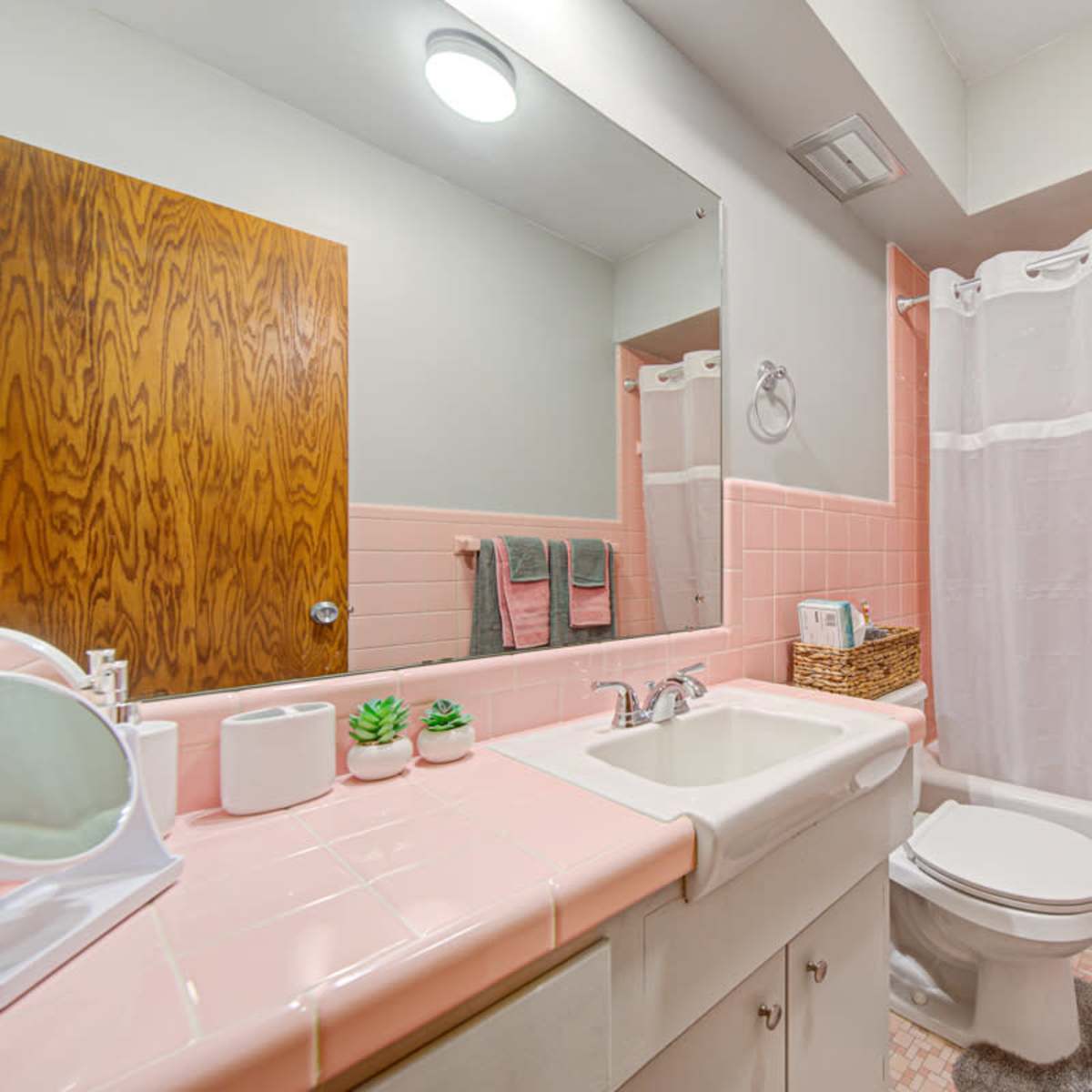 A small bathroom featuring pink tile accents, a white shower curtain, and basic fixtures including a sink and a toilet.
