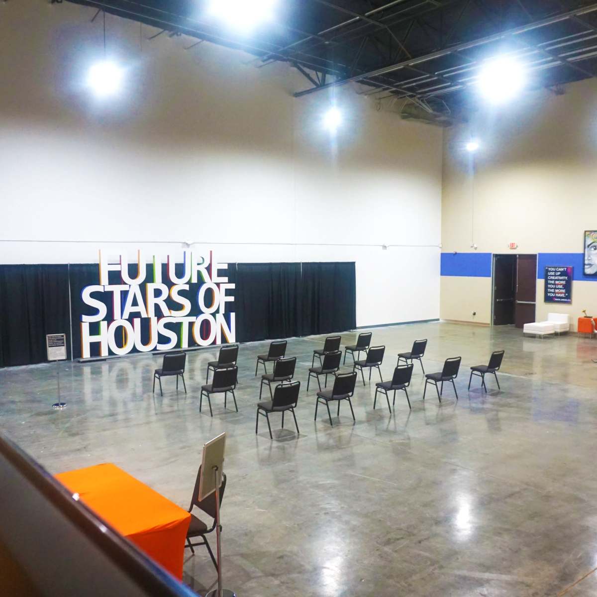 A spacious indoor venue with a sign reading "FUTURE STARS OF HOUSTON" and several chairs arranged in rows facing a presentation area.