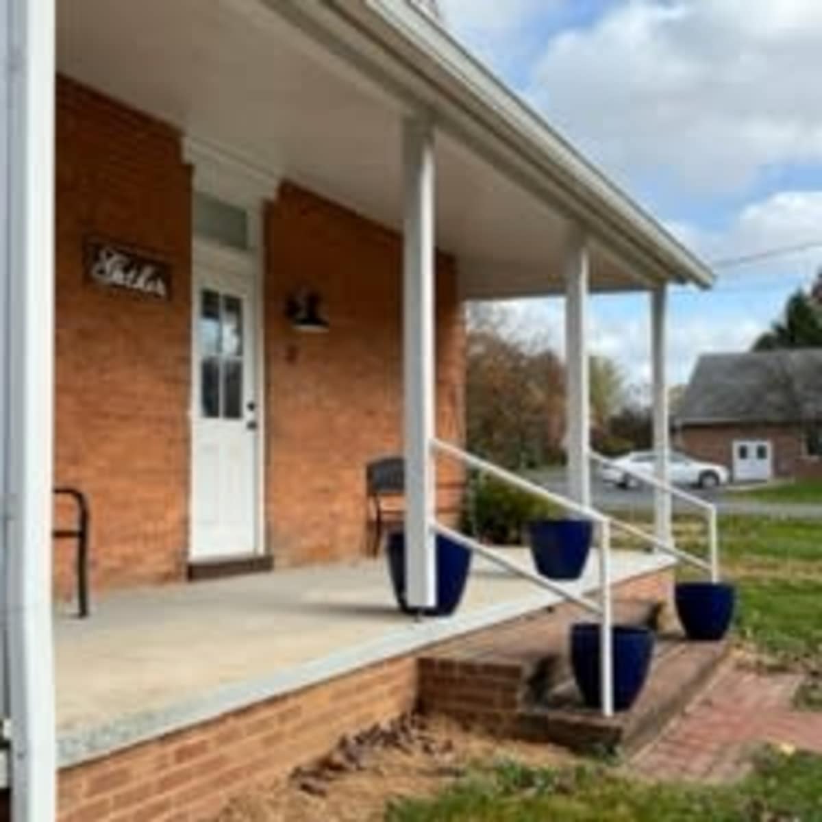 A brick house with a covered porch, featuring two benches and several blue flower pots on the steps.