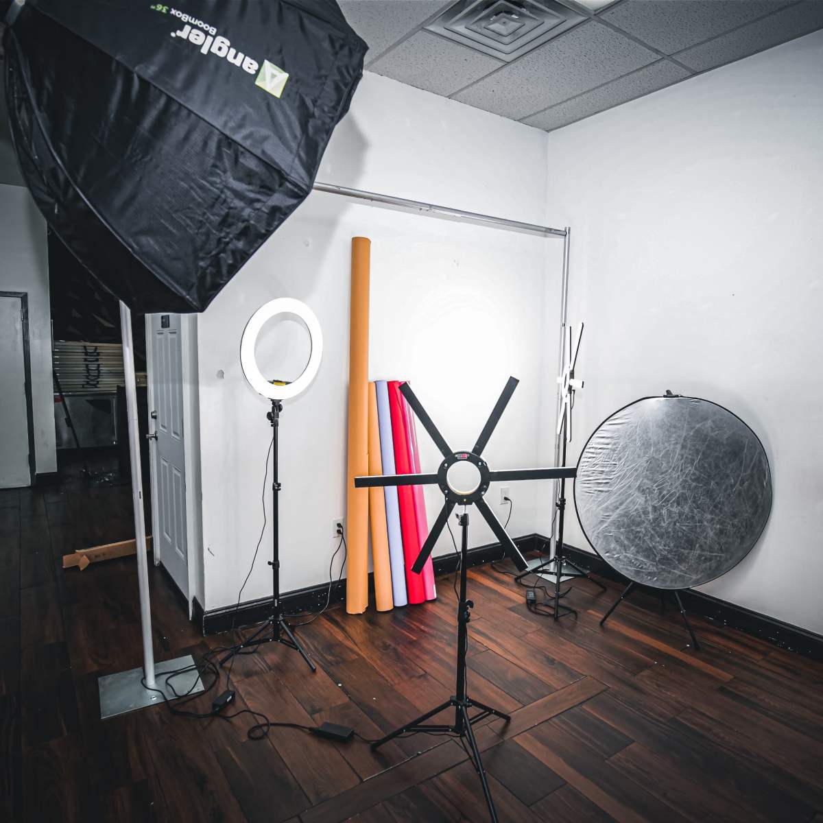 A photography studio setup with various lighting equipment and backdrops arranged against a white wall.