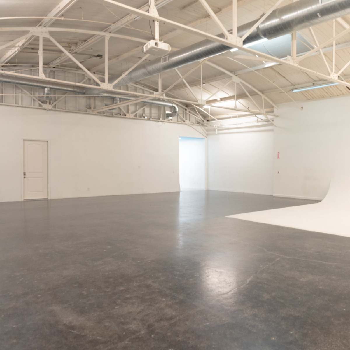 A spacious, empty studio with white walls, a curved backdrop, and a polished concrete floor.