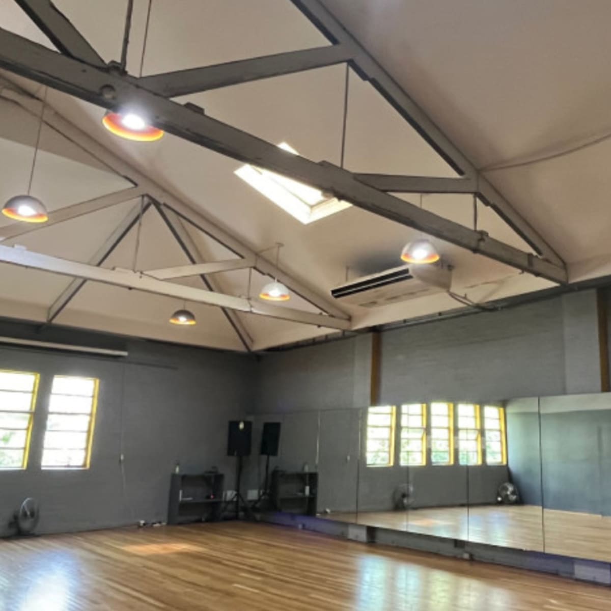 A bright studio space with high ceilings, large windows, and a mirrored wall.