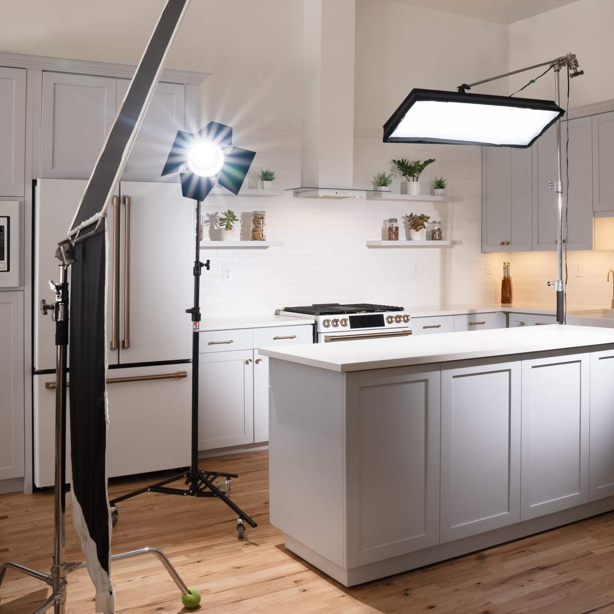 A modern kitchen is set up for a photoshoot with bright lights and equipment positioned around a central island.