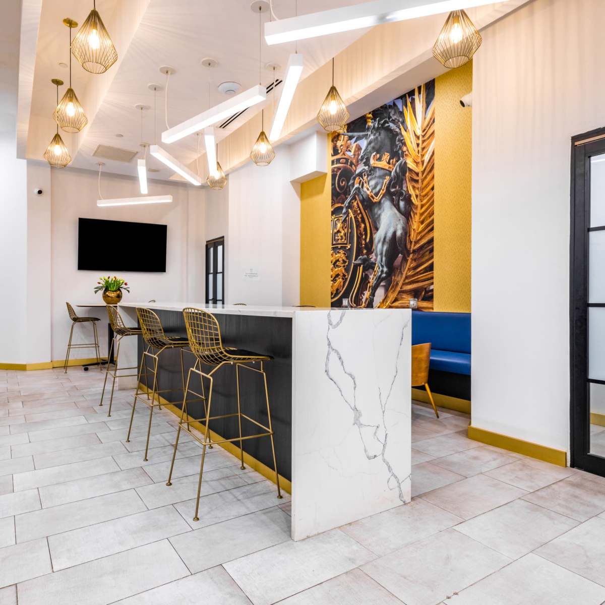 A modern kitchen or lounge area featuring a coffee station, high chairs at a bar-style table, and a large wall decoration with a horse portrait.