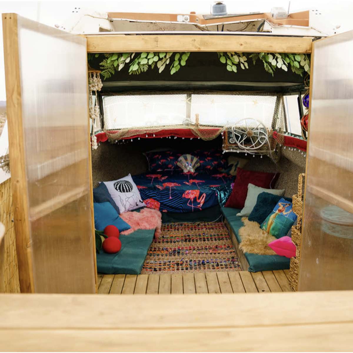 The interior of a rustic camper, featuring colorful cushions and a woven rug, set in a desert landscape.