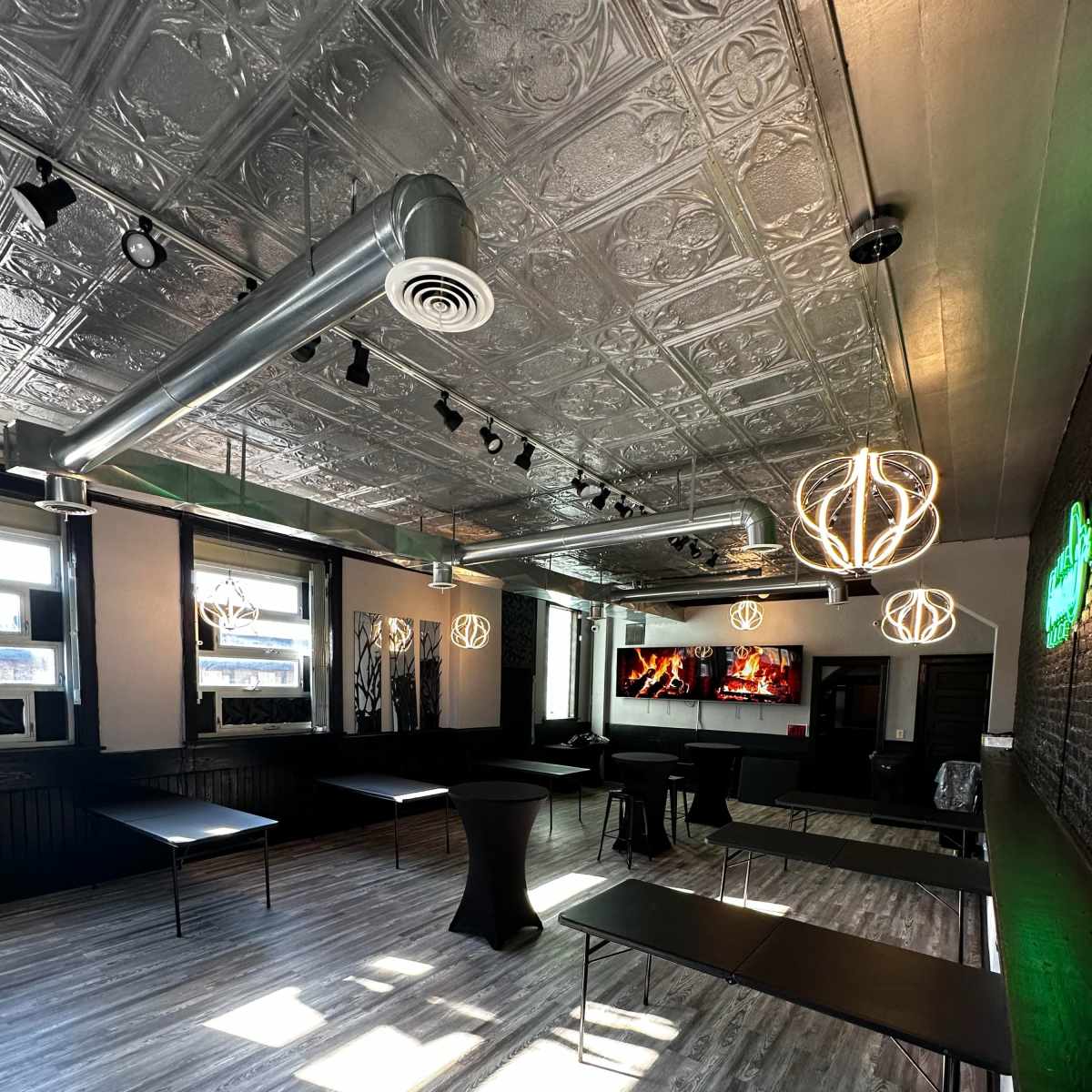 An empty event space with modern decor, featuring tables, bright lighting, and a large screen displaying a fire.