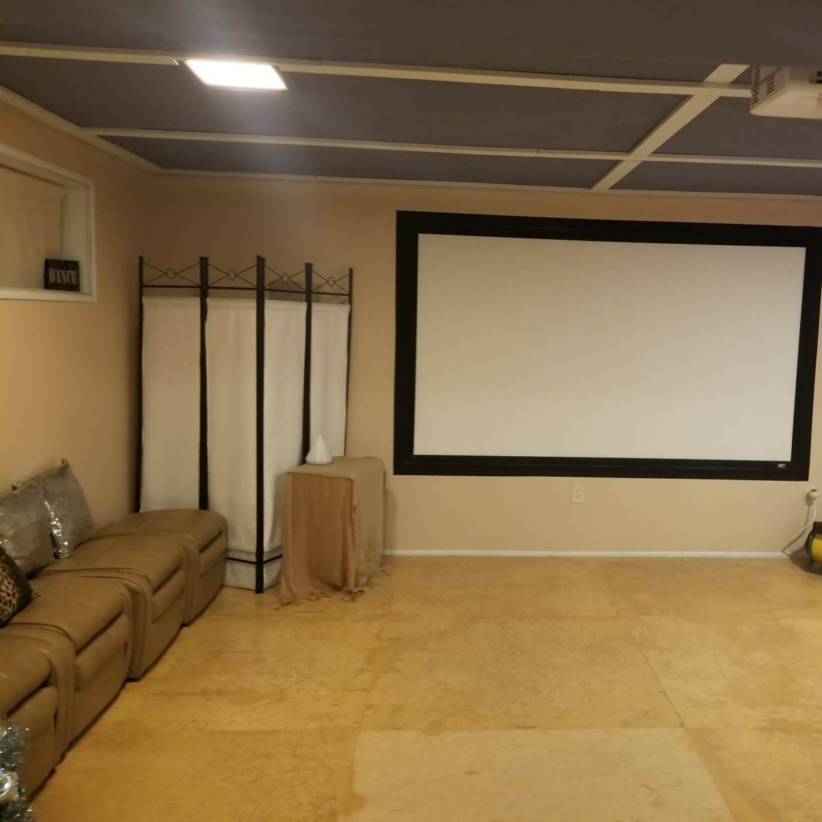 An empty room with a large projection screen on one wall, a sofa along another wall, and lighting equipment in the corner.