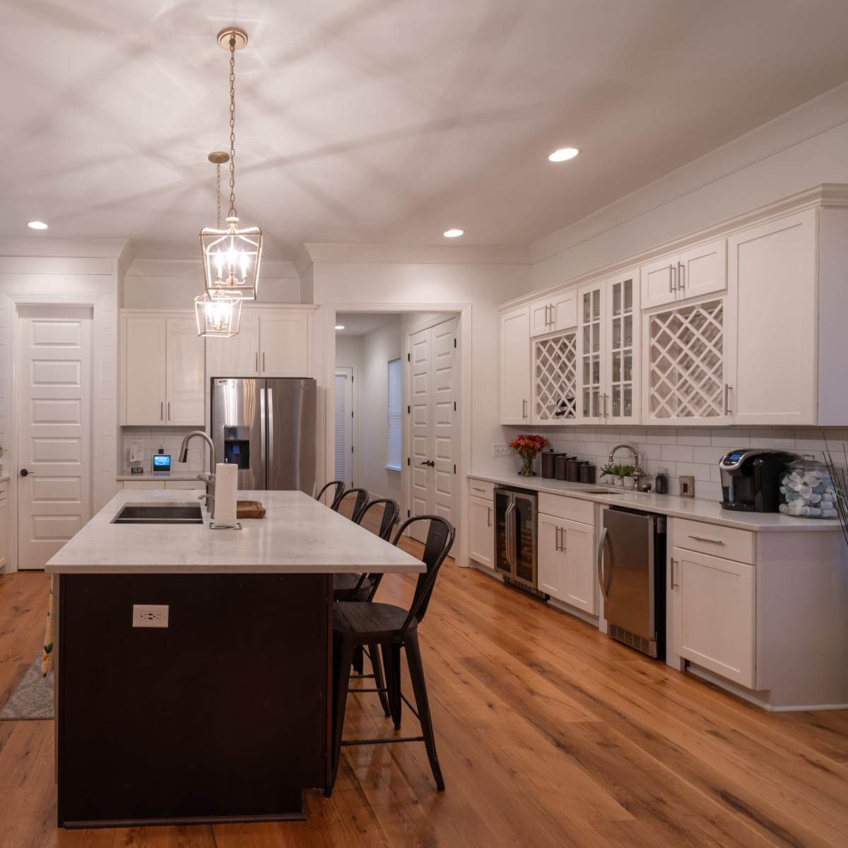 A modern kitchen with white cabinetry, a central island with seating, stainless steel appliances, and hardwood flooring.